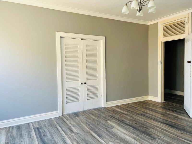An empty bedroom featuring modern laminate flooring, louvered closet doors, and neutral grey walls, providing a clean and versatile space.
