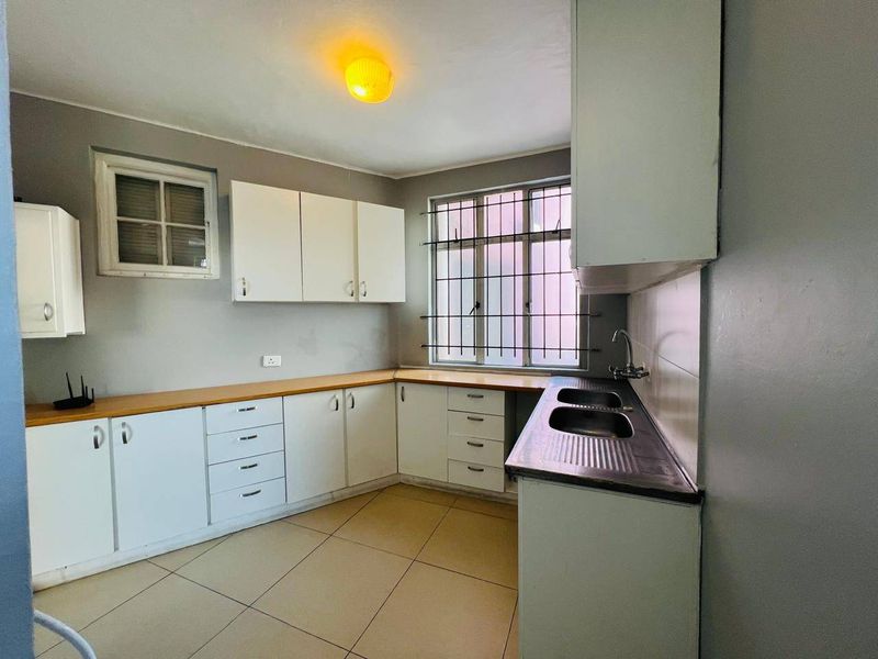 A functional kitchen featuring white built-in cabinetry, a double bowl sink, tiled flooring, and security bars on the windows.