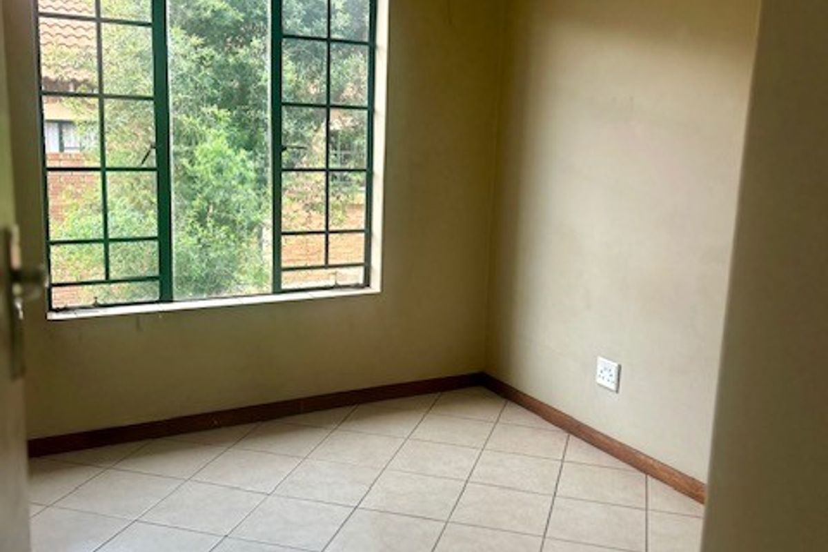 An empty bedroom featuring neutral tiled flooring, a large grid-pattern window, and plain walls, offering a blank canvas for personalization.