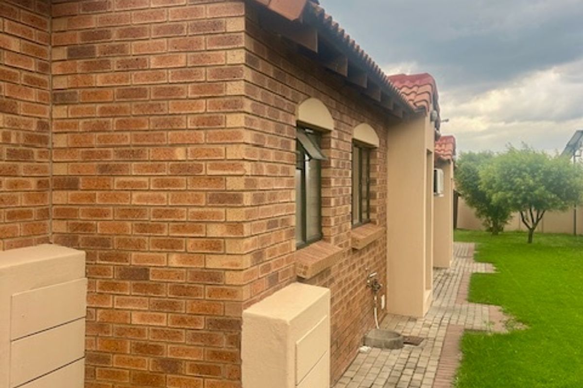 Rear exterior view of the townhouse featuring face brick walls, terracotta roof tiles, and a paved walkway adjacent to a lawn.