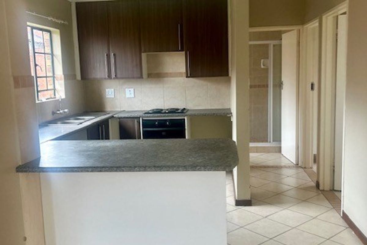 A functional kitchen featuring built-in cabinetry, a breakfast bar, and integrated appliances, with tiled flooring throughout and direct access to an adjacent bathroom area.