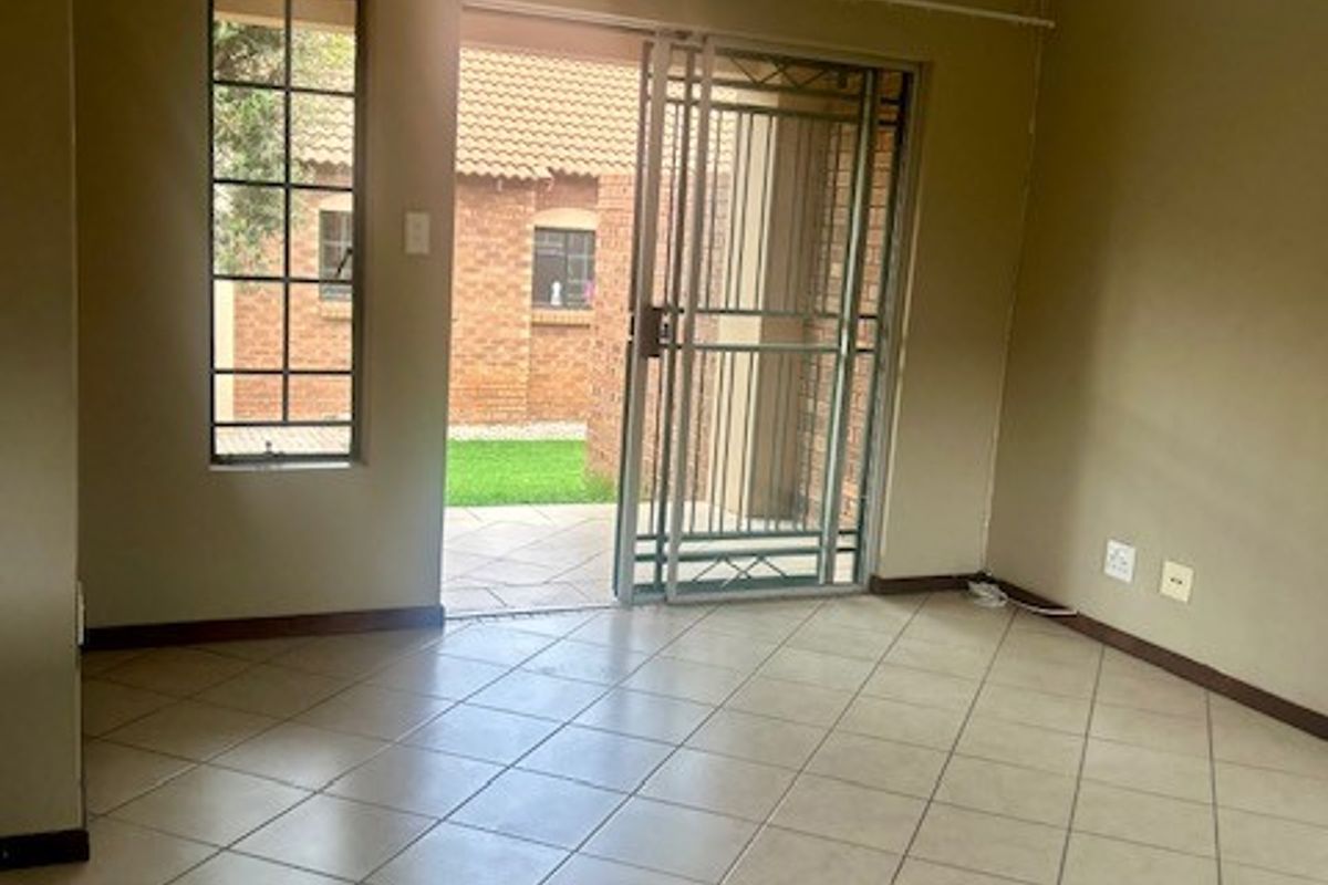 An empty living room featuring neutral tiled flooring, a sliding glass door with security gate, and access to an outdoor patio area.