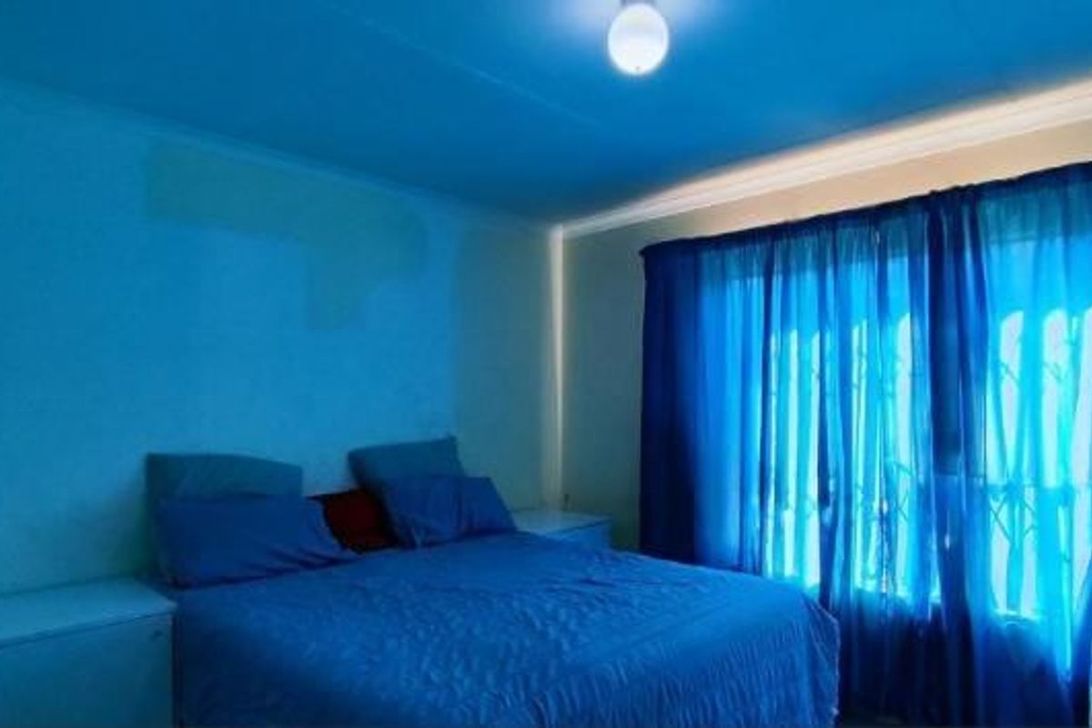 A bedroom featuring a window with curtains and a ceiling light fixture, currently showing signs of uneven wall paint.