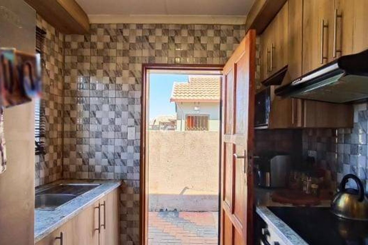 A functional kitchen featuring built-in cabinetry, a hob with an extractor fan, and a double sink, with direct access to an outdoor paved area.