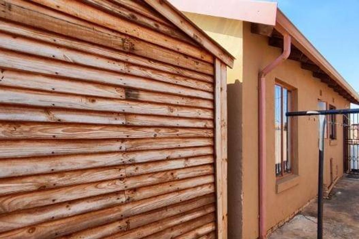 Side exterior view of the property featuring timber cladding, plastered walls, and a paved walkway leading to a security gate.