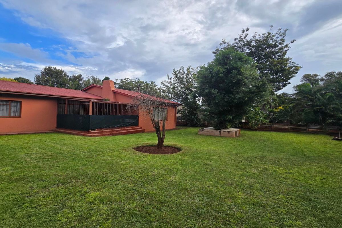 Spacious rear garden featuring a well-maintained lawn, mature trees, and a covered patio area attached to the main house structure.