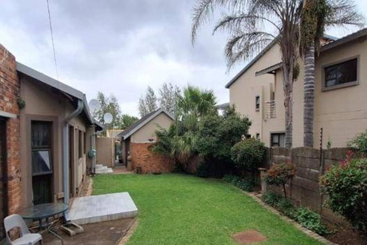 A rear garden area featuring a lawn, paved patio section, and exposed brick exterior walls with sliding door access to the main dwelling.