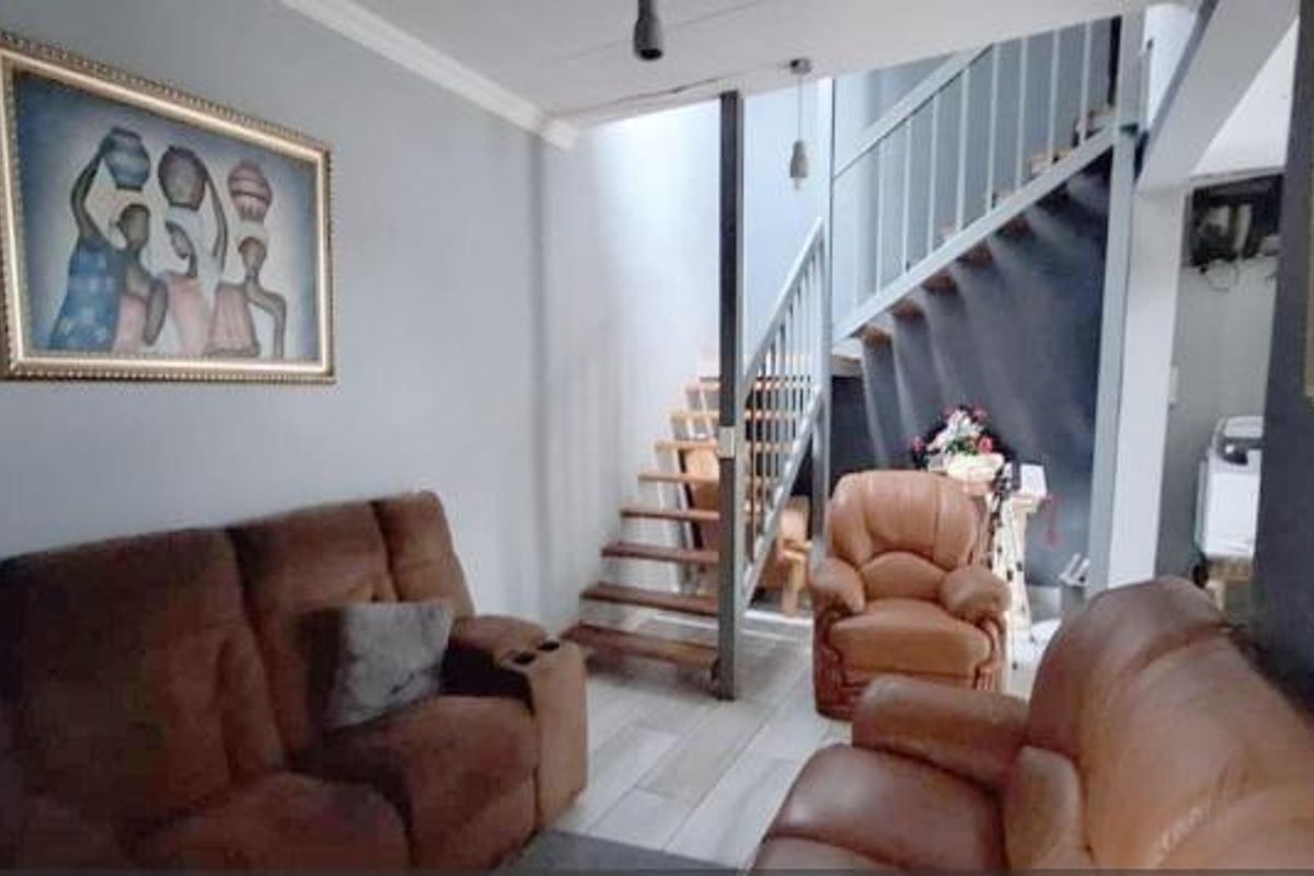 A living room area featuring a staircase with a metal balustrade and tiled flooring, providing access to the upper level.