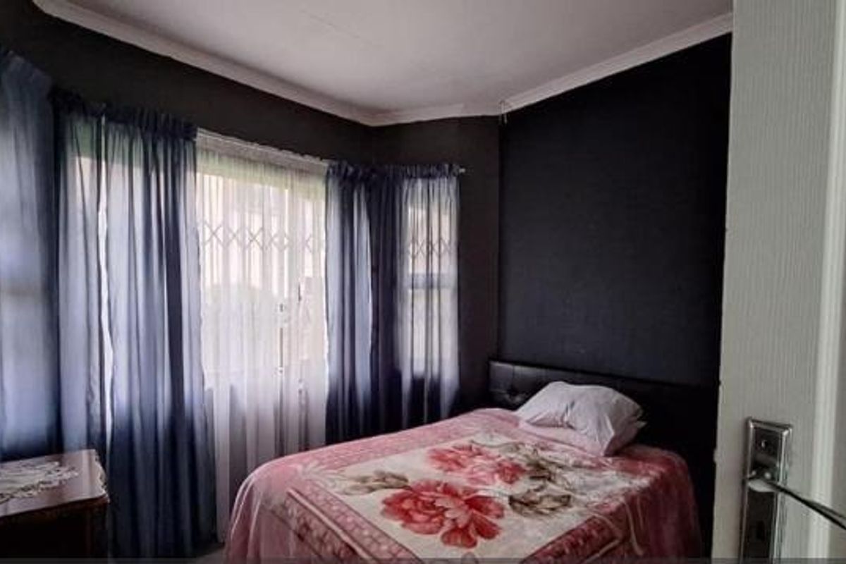 A bedroom featuring a bay window with security bars and dark-toned walls, offering a cozy and private sleeping space.