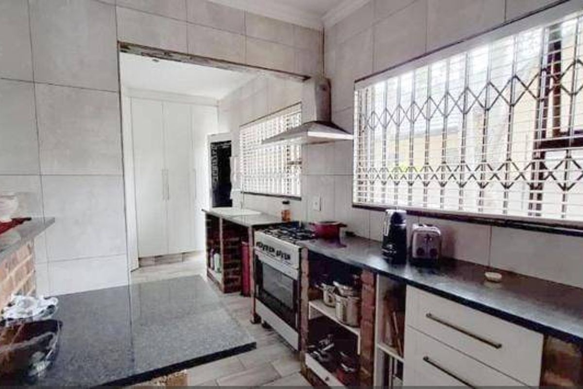 A functional kitchen featuring granite countertops, a gas stove with extractor fan, and tiled wall finishes with integrated storage cabinetry.