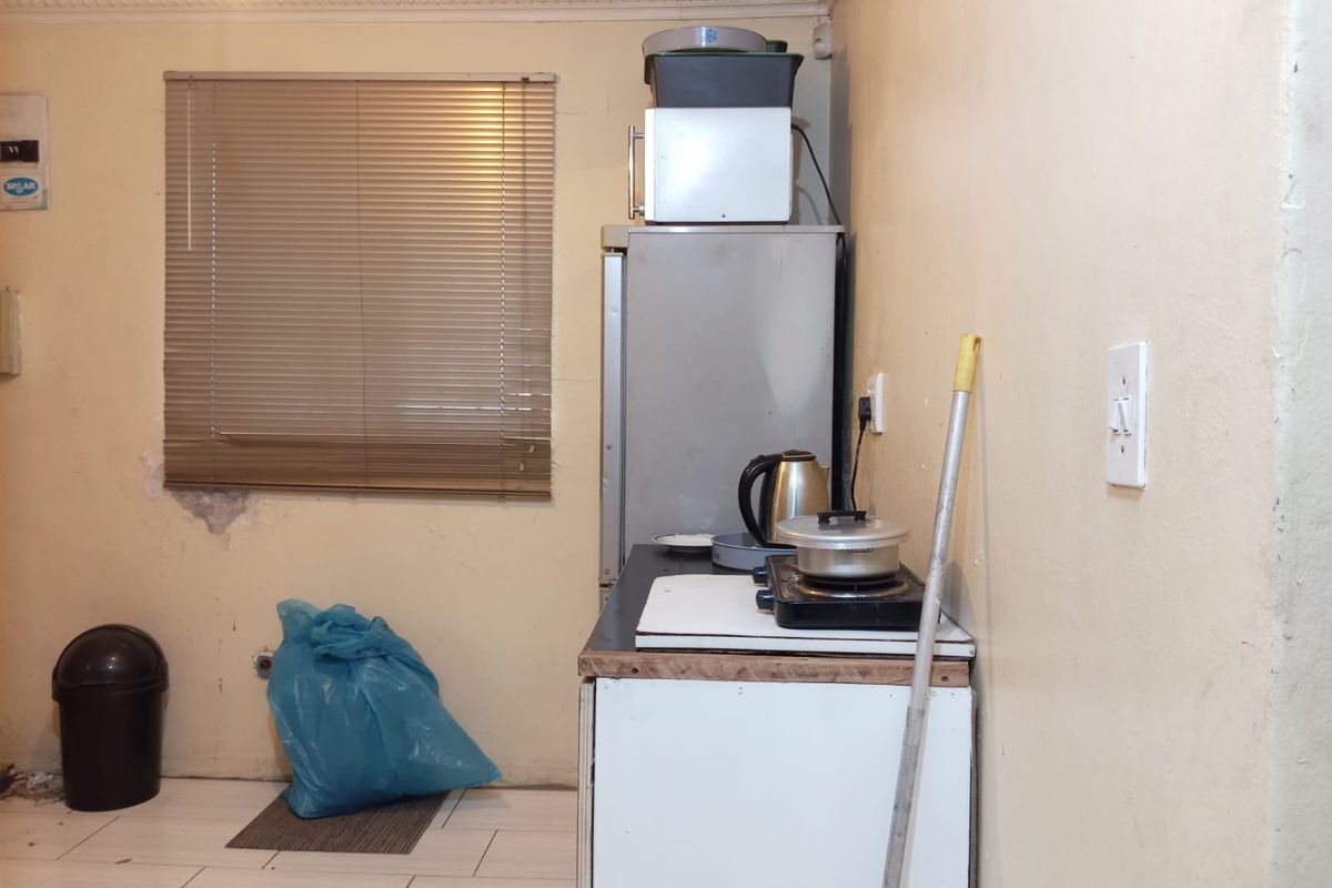A small kitchen area featuring tiled floors, a window with venetian blinds, and basic base cabinetry requiring maintenance and cosmetic updates.
