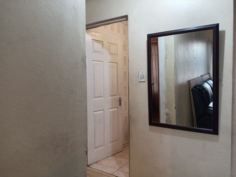 A simple hallway area featuring a panelled door and plain wall finishes, showing signs of wear and requiring cosmetic attention.