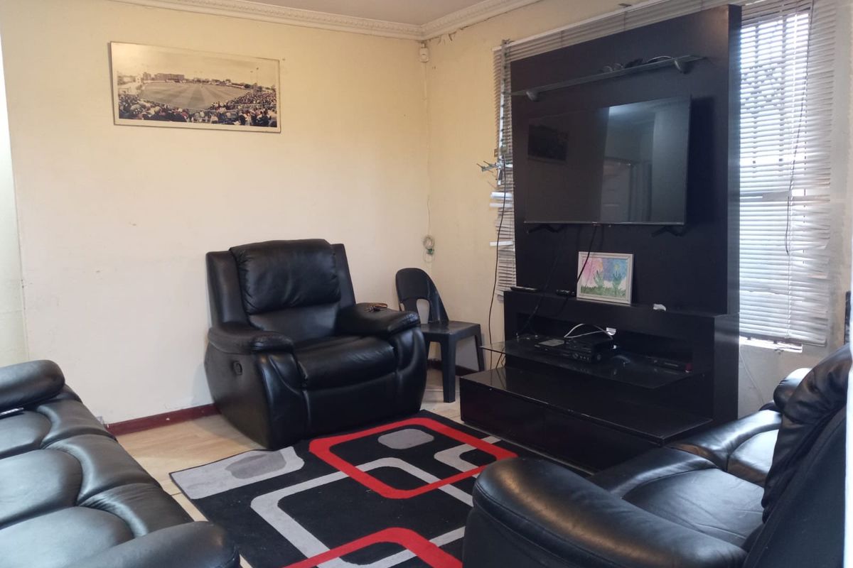 A living room featuring crown molding and venetian blinds, showing signs of wear on the walls requiring cosmetic attention.