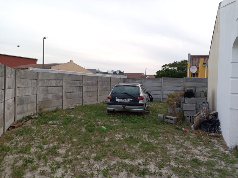 A rear yard area enclosed by precast concrete boundary walls, featuring an unmaintained lawn and space for outdoor storage.