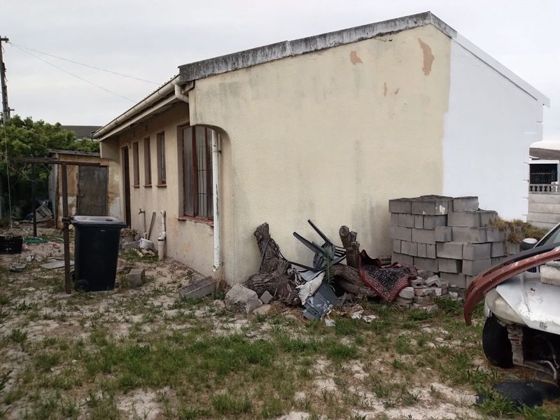 Rear exterior view of the property showing significant wear to the facade, peeling paint, and unmaintained surrounding grounds.