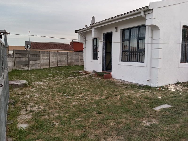 Rear view of the property featuring a small yard, precast concrete boundary wall, and security-fitted windows.