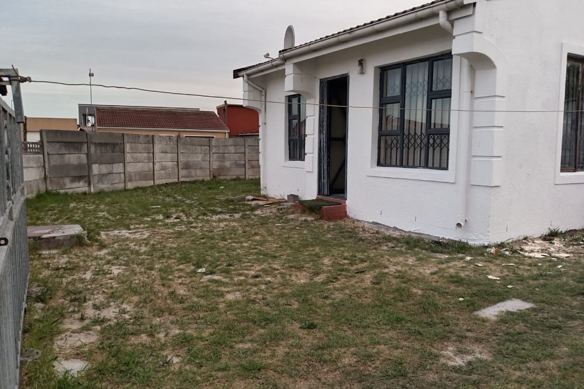 Rear view of the property featuring a small yard, precast concrete boundary wall, and security-fitted windows.