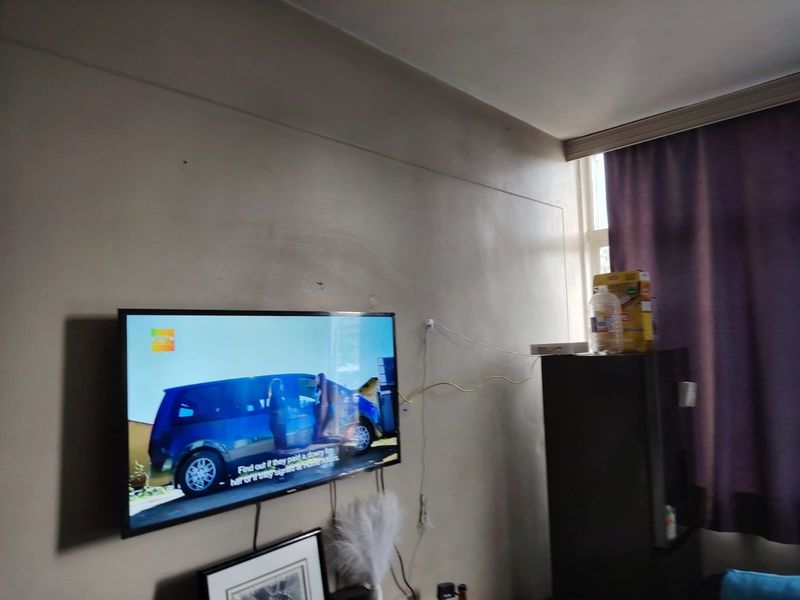 A living room area featuring wall-mounted television space and window with curtain rail, requiring minor cosmetic updates to wall finishes and cable management.