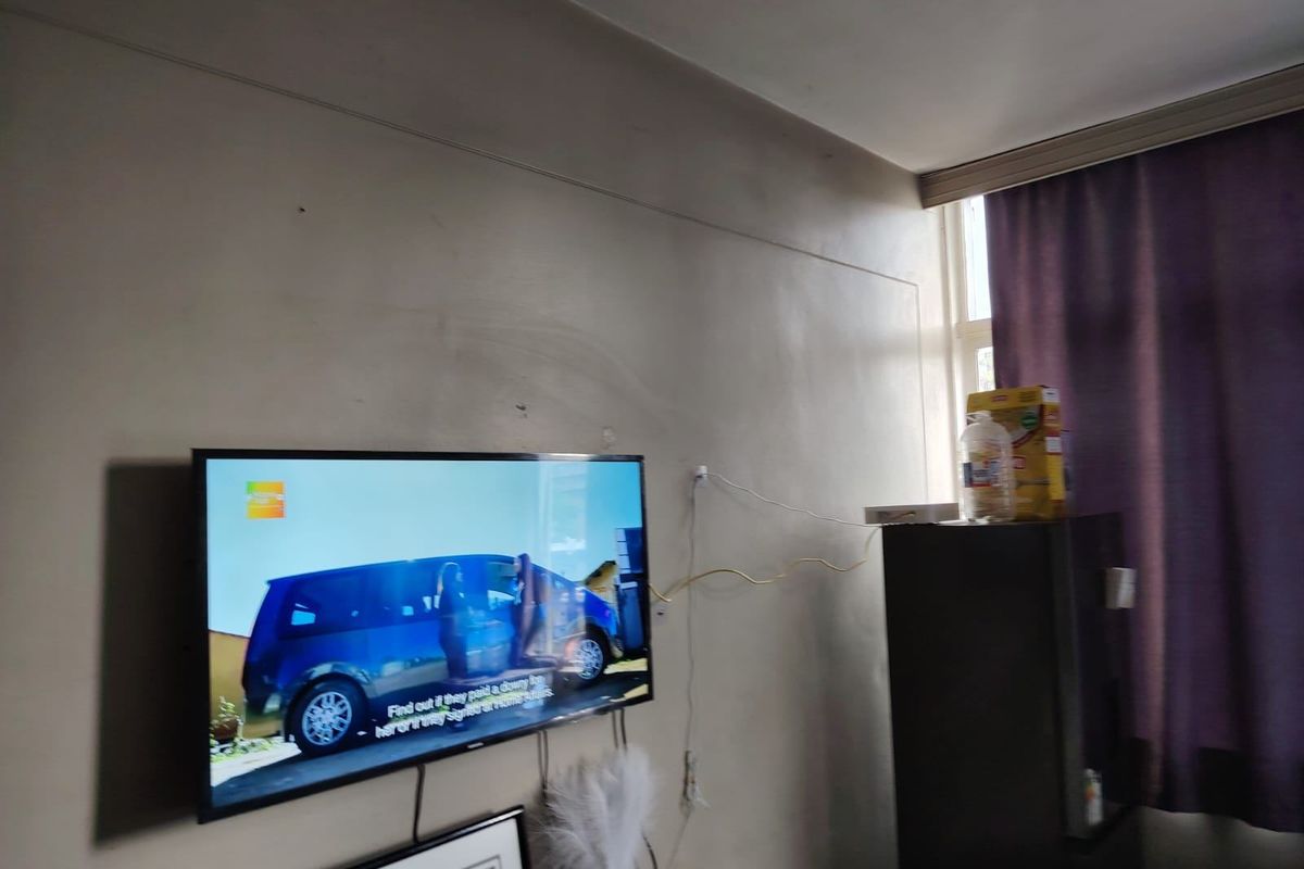 A living room area featuring wall-mounted television space and window with curtain rail, requiring minor cosmetic updates to wall finishes and cable management.