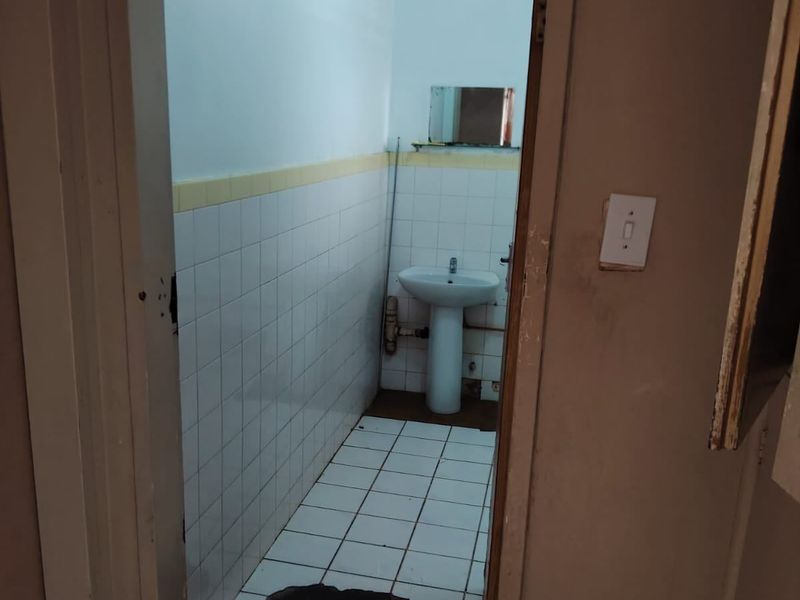 A small bathroom featuring a pedestal basin and tiled finishes, currently requiring maintenance and repair to the flooring and fixtures.