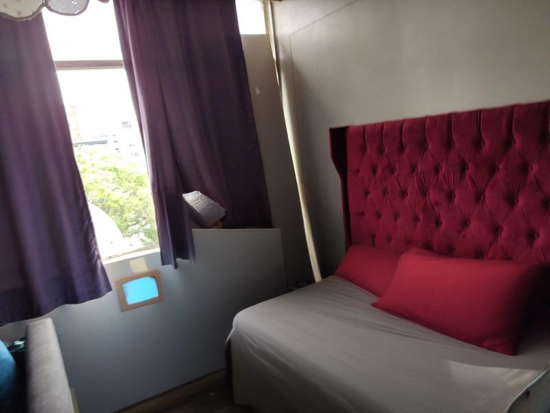 A compact bedroom featuring a large window and neutral wall finishes, requiring minor cosmetic updates to improve the overall aesthetic and finish quality.