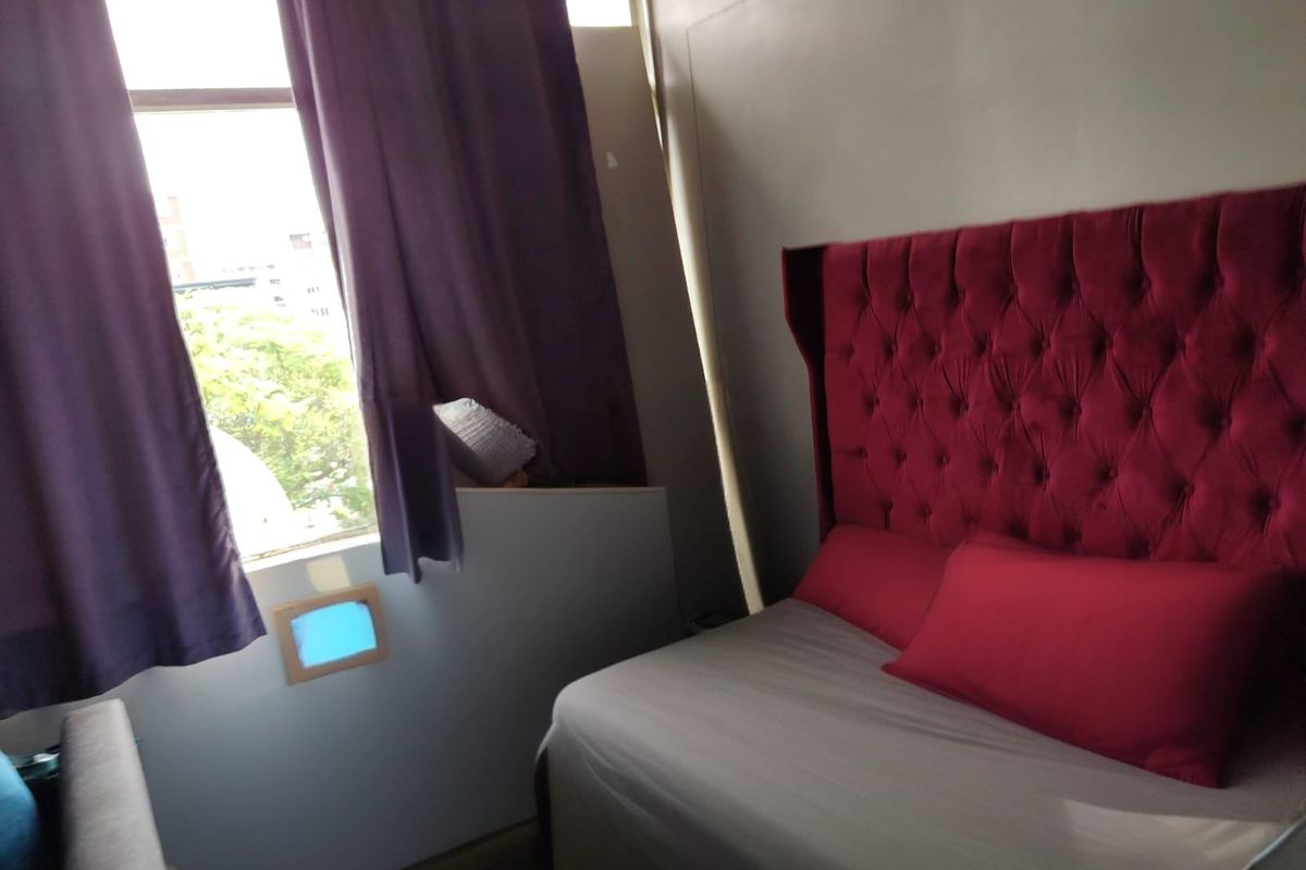 A compact bedroom featuring a large window and neutral wall finishes, requiring minor cosmetic updates to improve the overall aesthetic and finish quality.