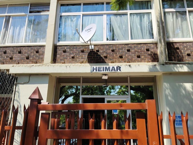 Front entrance view of Heimar apartment building featuring a brick facade, metal security gate, and aluminum window frames.