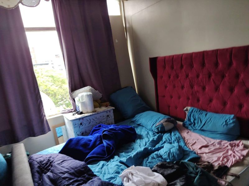 A bedroom featuring a large window with curtains and space for a double bed.