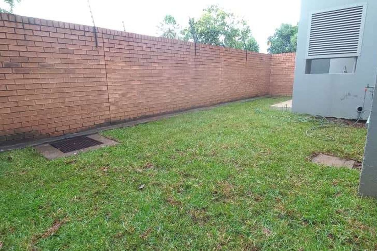 A private rear garden area featuring a brick boundary wall with electric fencing and a small lawn space adjacent to the building exterior.