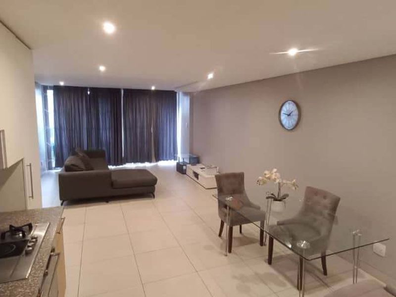 Modern open-plan living area featuring a sleek kitchen with built-in gas hob, tiled flooring, and recessed lighting, flowing into a spacious lounge and dining area.