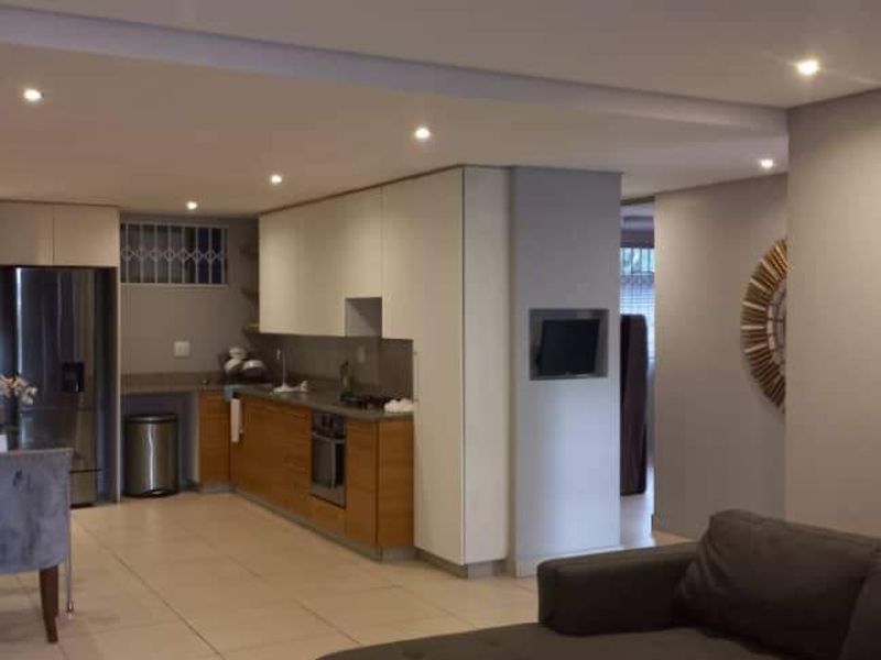 Modern open-plan living area featuring a sleek kitchen with built-in cabinetry, integrated appliances, and recessed downlighting throughout the space.