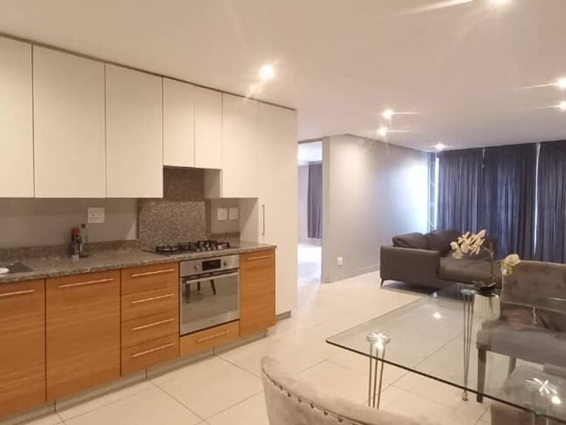 Modern open-plan kitchen and living area featuring wood-finish cabinetry, granite countertops, integrated appliances, and tiled flooring throughout.