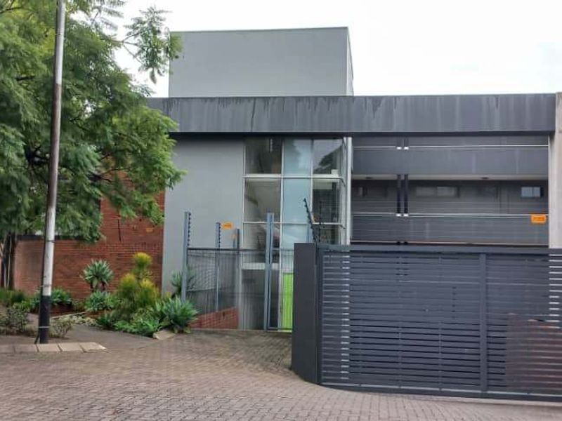 Front exterior view of the apartment complex featuring a secure gated entrance, brick and rendered facade, and paved driveway access.