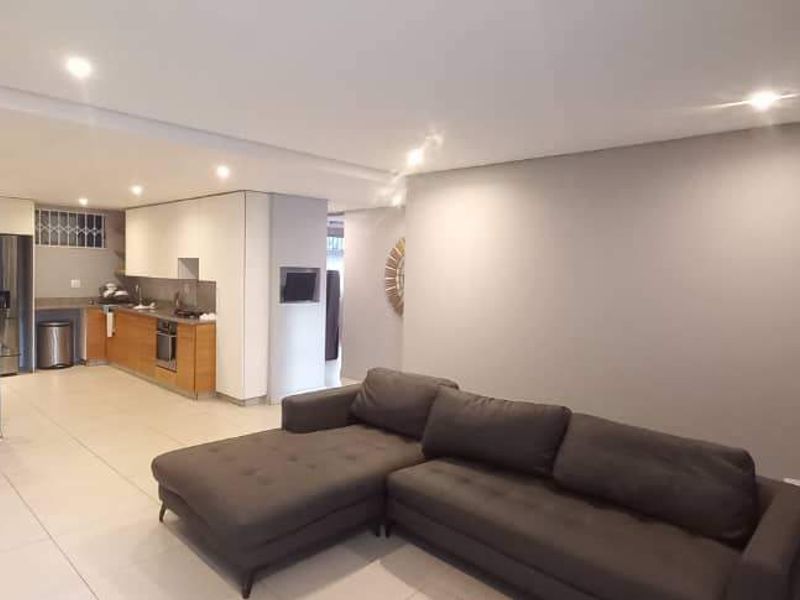 An open-plan living and kitchen area featuring modern tiled flooring, recessed ceiling lights, and a functional kitchen layout with built-in cabinetry and appliances.