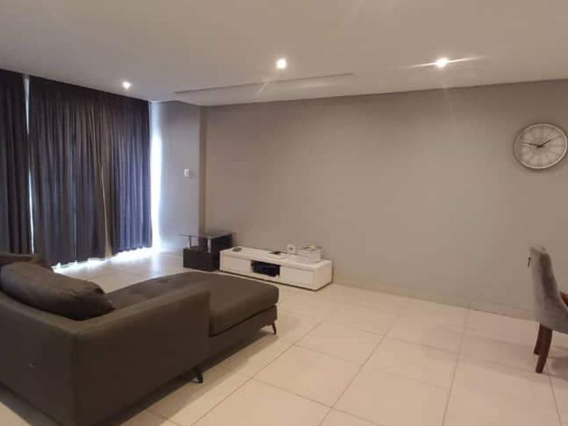 Spacious open-plan living and dining area featuring neutral tiled flooring, recessed downlighting, and large windows with full-length curtains.