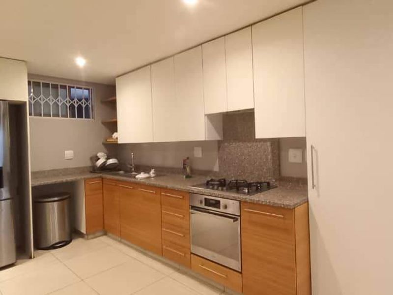 Modern kitchen featuring light wood and white cabinetry, stone countertops, built-in oven, gas hob, and tiled flooring in an open-plan layout.