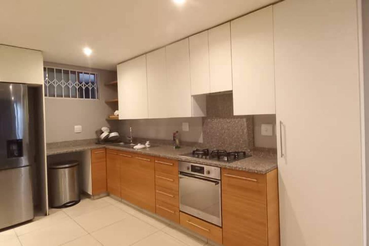 Modern kitchen featuring light wood and white cabinetry, stone countertops, built-in oven, gas hob, and tiled flooring in an open-plan layout.