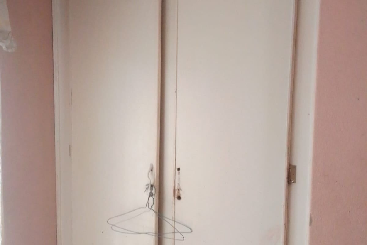 A bedroom featuring a built-in wardrobe with visible wear and tear on the door frames and finish.