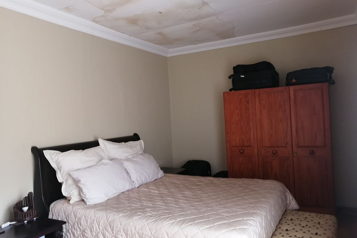 A bedroom featuring a built-in wooden wardrobe and visible water damage on the ceiling.