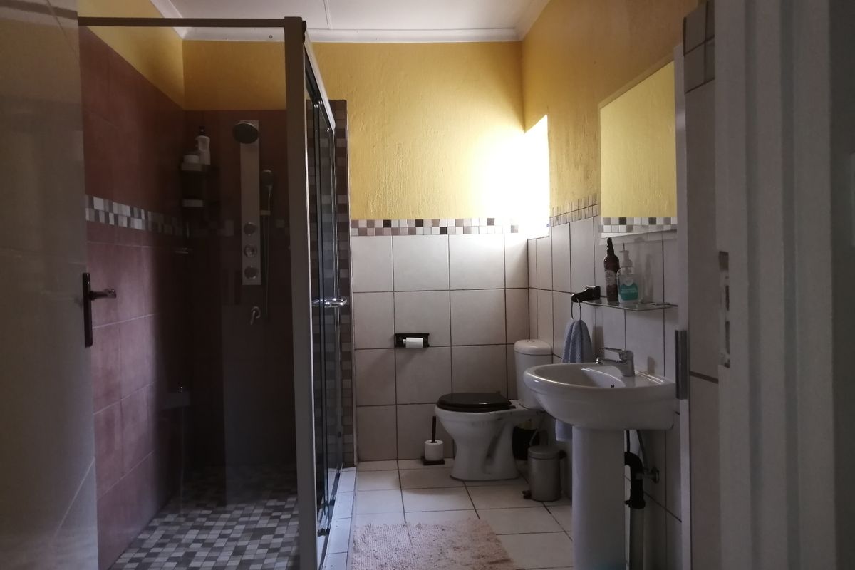 A functional bathroom featuring a shower enclosure, pedestal basin, and toilet with tiled walls and flooring.