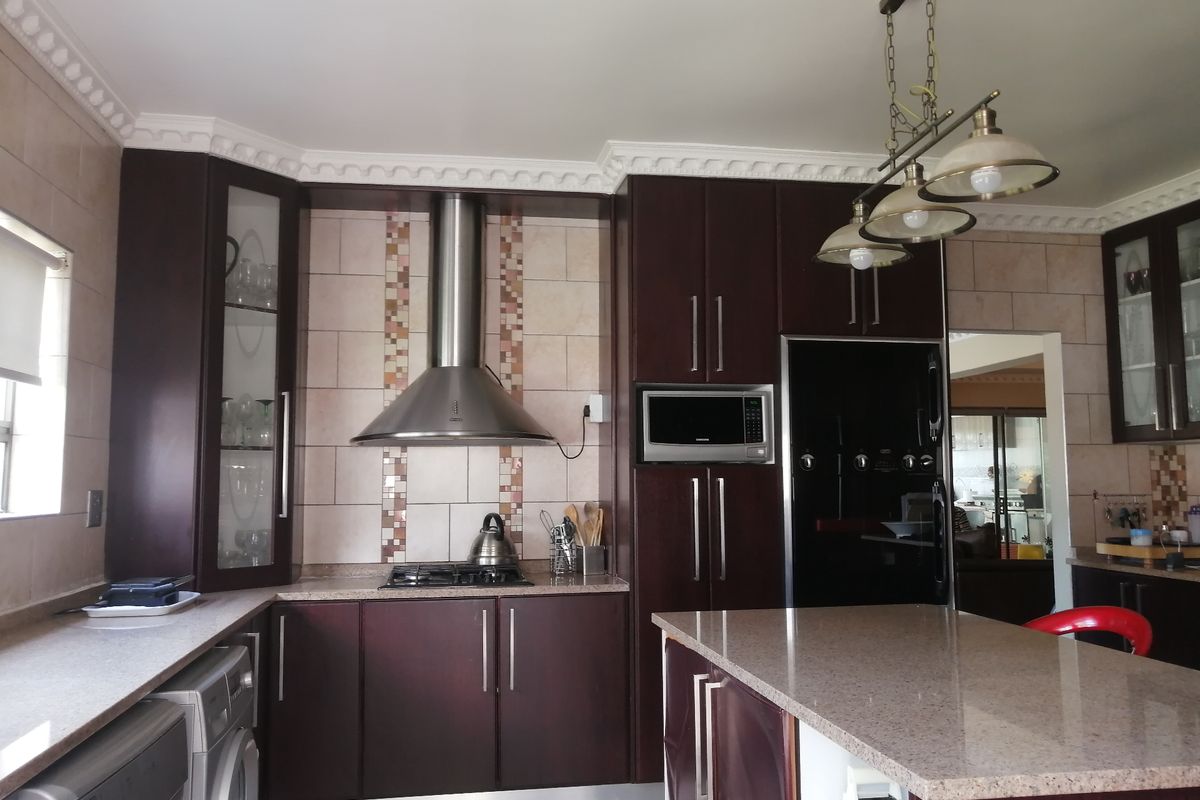 A well-appointed kitchen featuring dark wood cabinetry, granite countertops, a gas hob with stainless steel extractor, and a central island with pendant lighting.