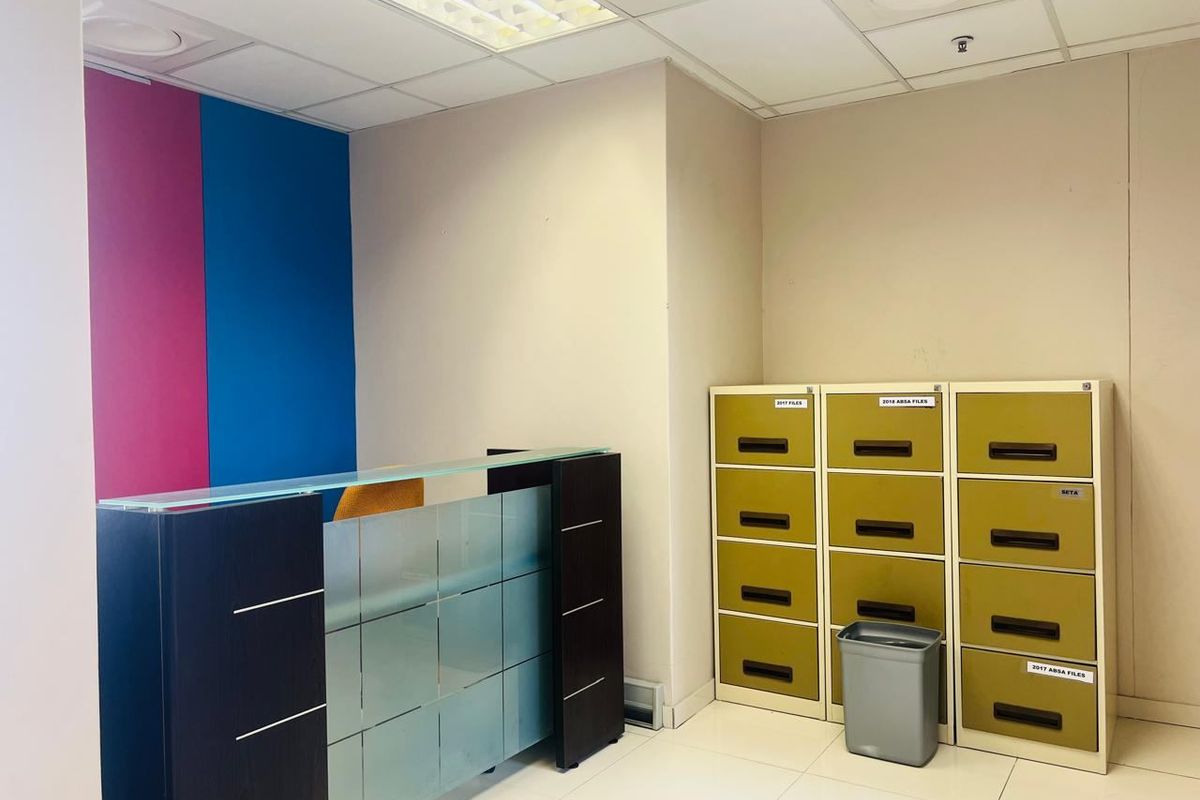 A commercial office space featuring a modern reception desk, tiled flooring, and a suspended ceiling with integrated lighting.