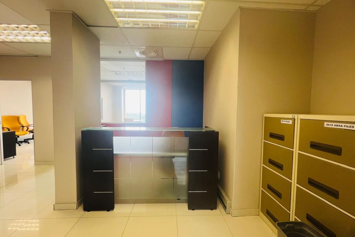 A commercial office space featuring a built-in reception desk, tiled flooring, and a suspended ceiling with recessed lighting.