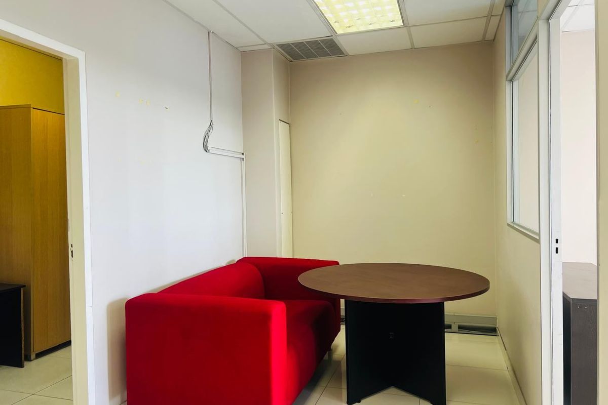 A compact commercial office space featuring tiled flooring, a suspended ceiling with integrated lighting, and a glass partition wall.