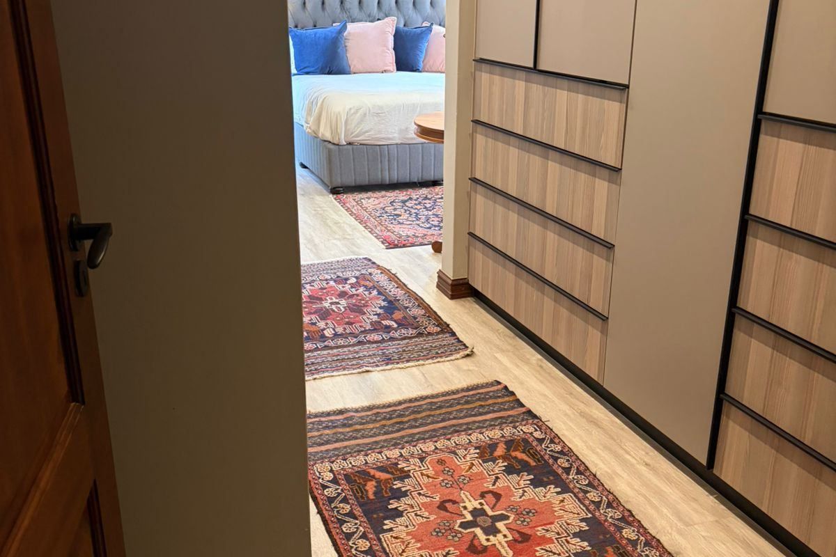 A well-maintained bedroom featuring modern built-in cupboards with a sleek finish and light-toned laminate flooring, leading into a comfortable sleeping area.