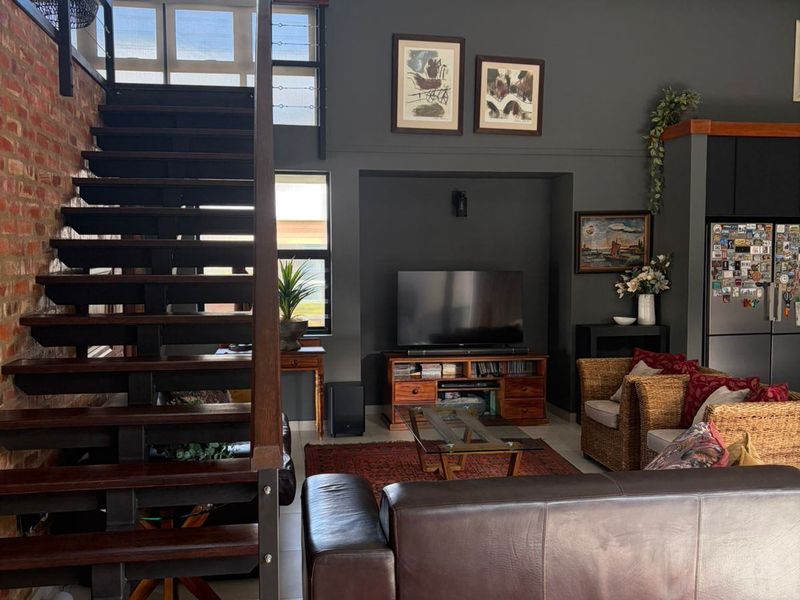 Spacious open-plan living area featuring a striking timber staircase, vaulted ceilings with exposed beams, and a feature exposed brick wall.