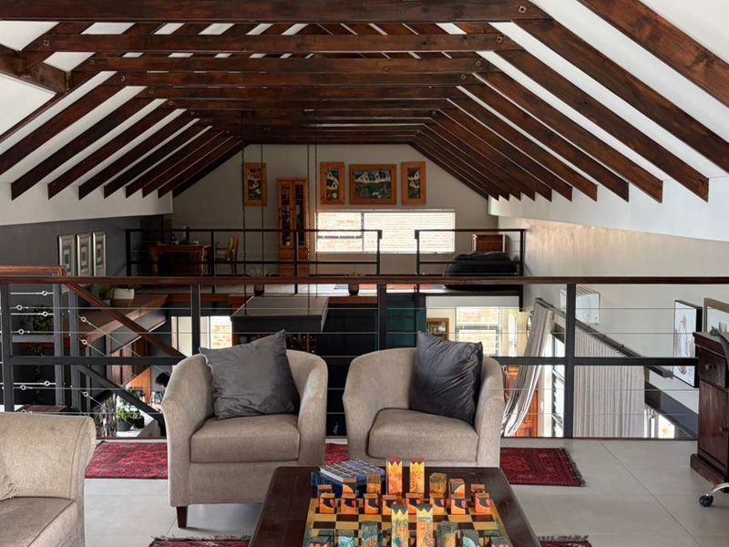 Spacious living area featuring high vaulted ceilings with exposed timber trusses, a mezzanine level, and modern metal balustrades overlooking the lower floor.