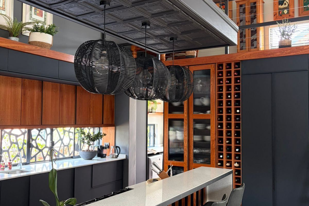 Modern kitchen featuring a large island with stone countertops, custom dark cabinetry, integrated wine storage, and a striking vaulted ceiling with exposed timber beams.