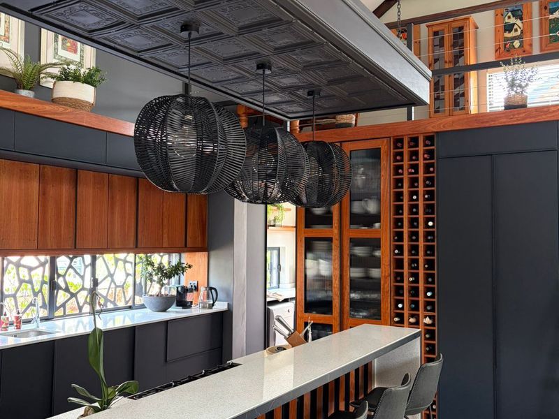 Modern kitchen featuring a large island with stone countertops, custom dark cabinetry, integrated wine storage, and a striking vaulted ceiling with exposed timber beams.