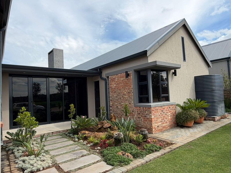 A well-maintained rear exterior view featuring a modern blend of brick and plaster finishes, aluminium glazing, and a landscaped garden with a paved walkway.